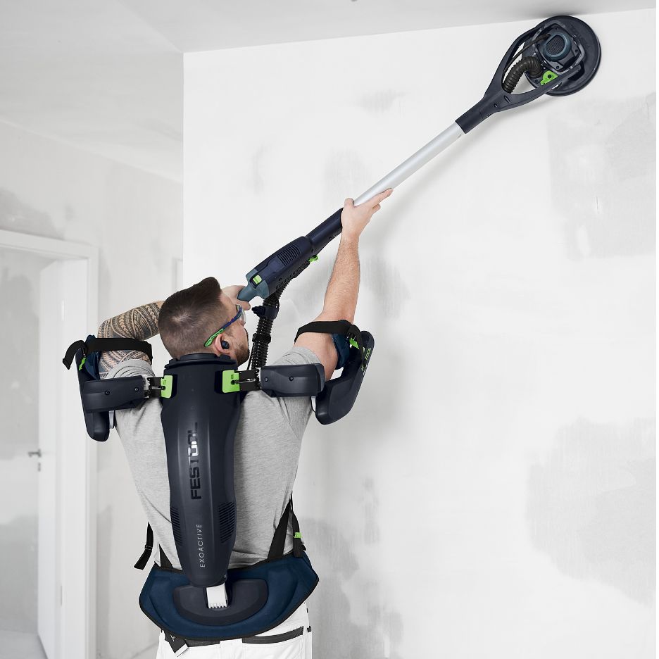 Man wearing Festool Exoskeleton ExoActive EXO 18 HPC 4.0 I-Plus while sanding wall